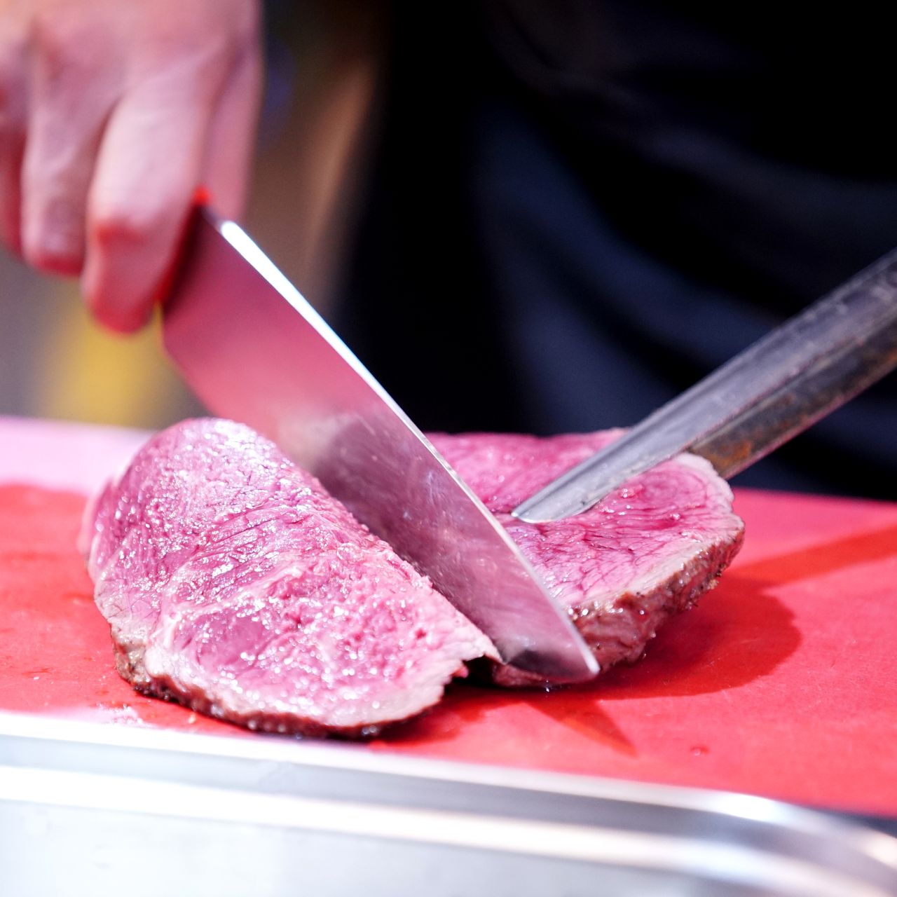 Chef slices a piece of roast beef on a red cutting board with a sharp knife