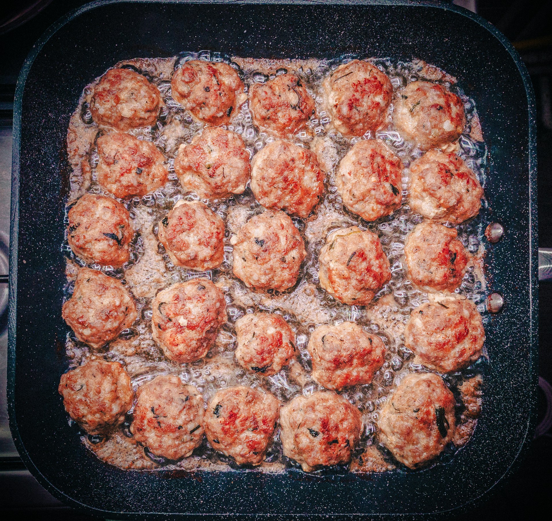 Meatballs are frying in a pan with bubbling oil