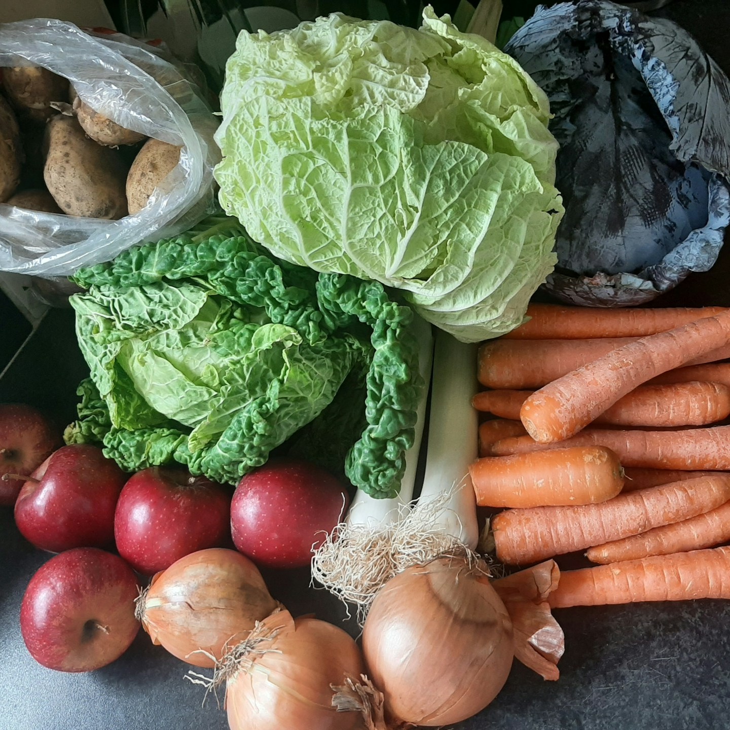 A variety of fresh vegetables and apples are arranged on a countertop, ready for meal preparation