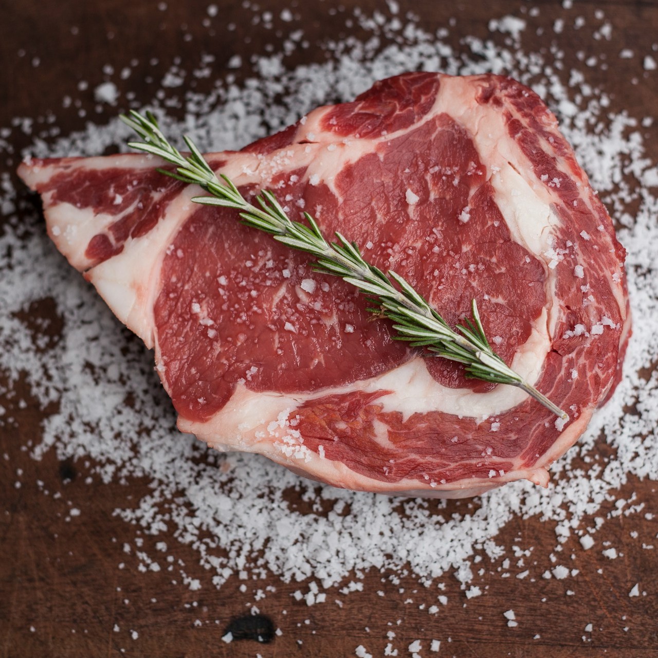 Raw steak with rosemary and salt on a wooden surface