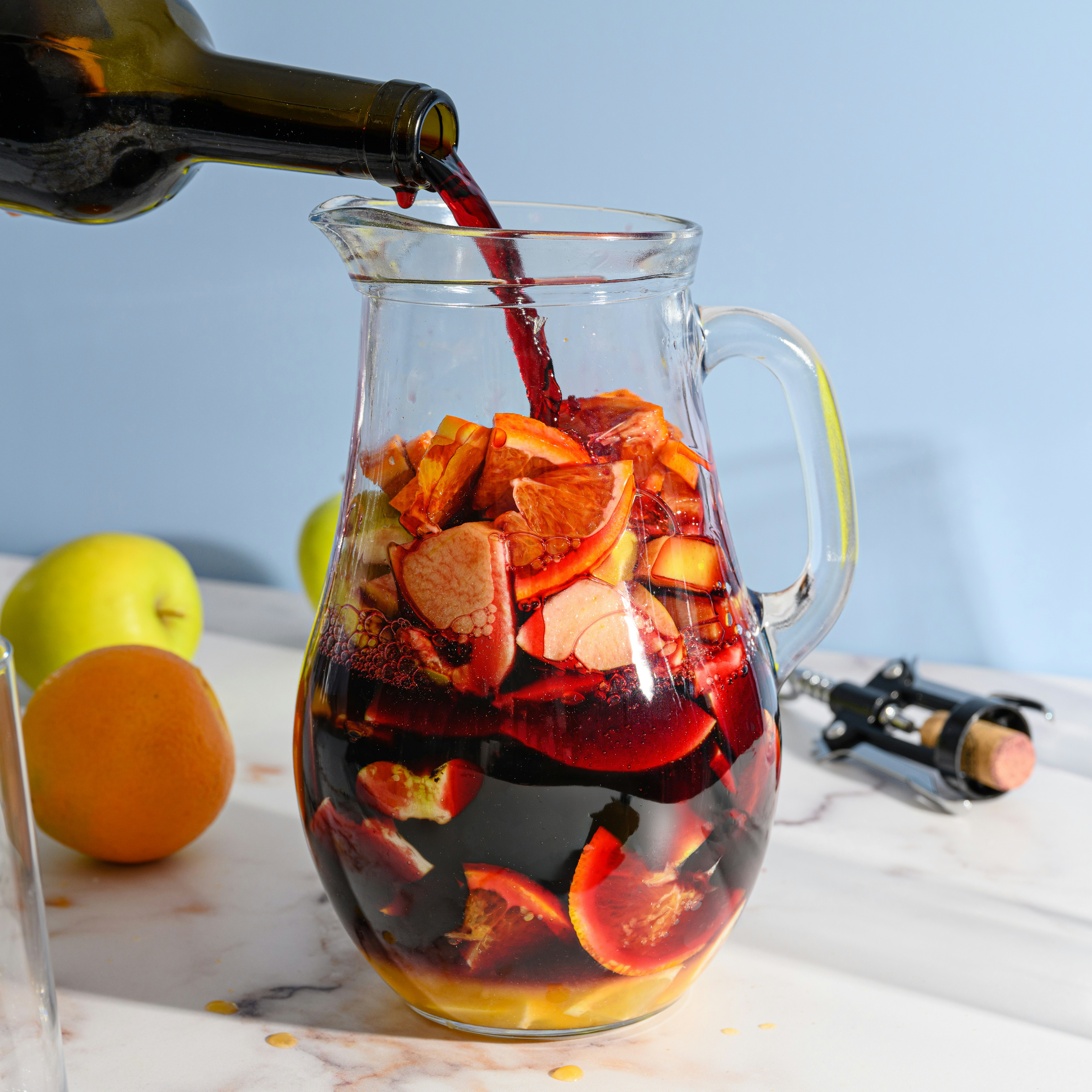 Red wine is poured into a pitcher filled with sliced fruits for sangria