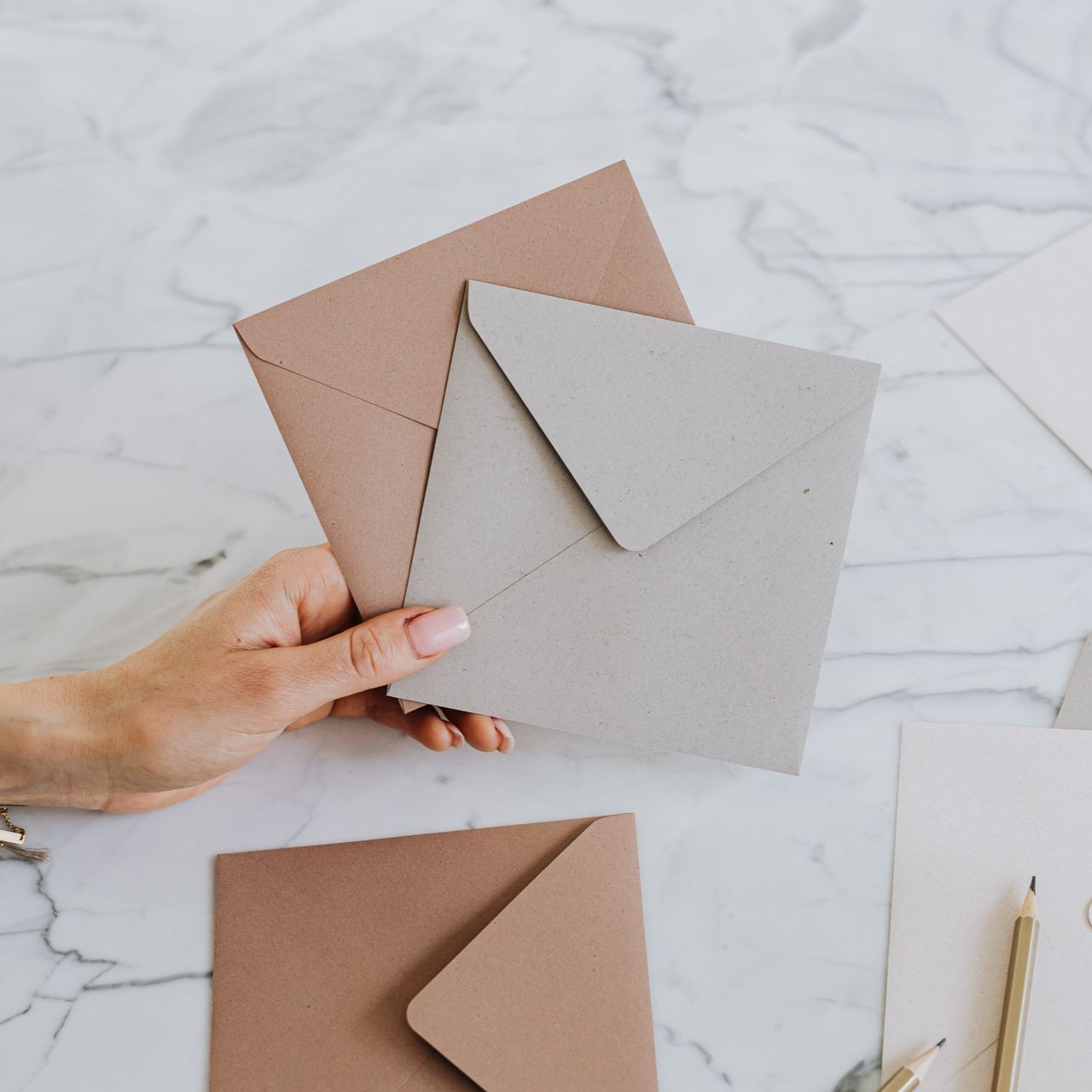 A hand holds two blank envelopes containing invitations on a marble surface