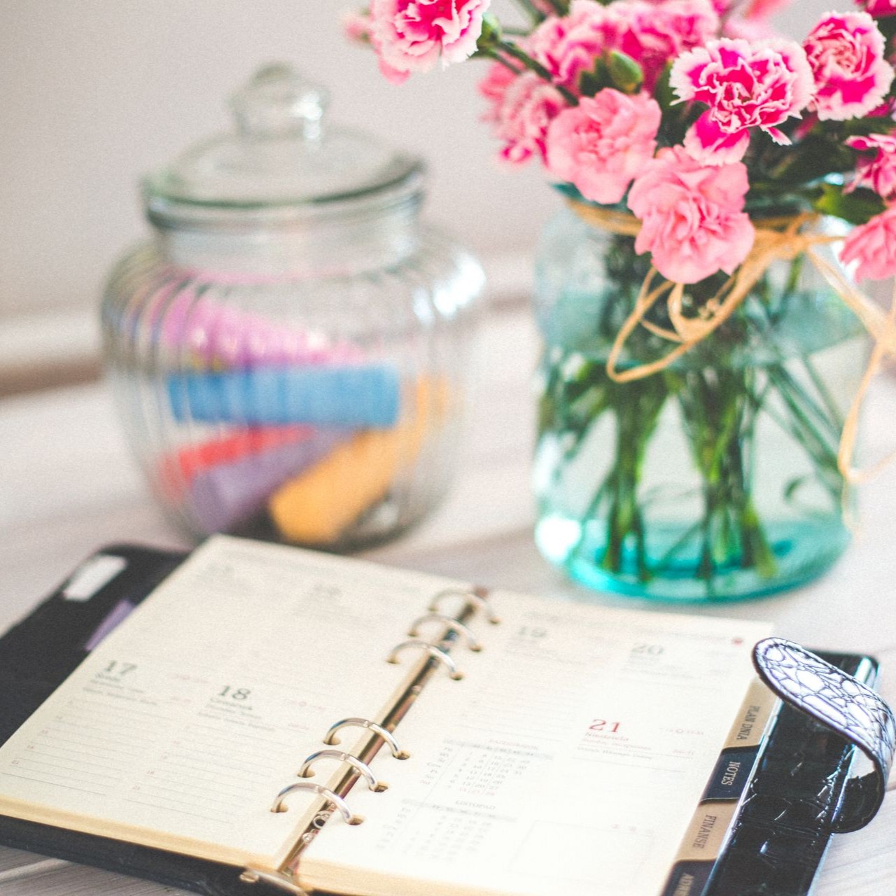 Open planner on a table with a jar of pink flowers