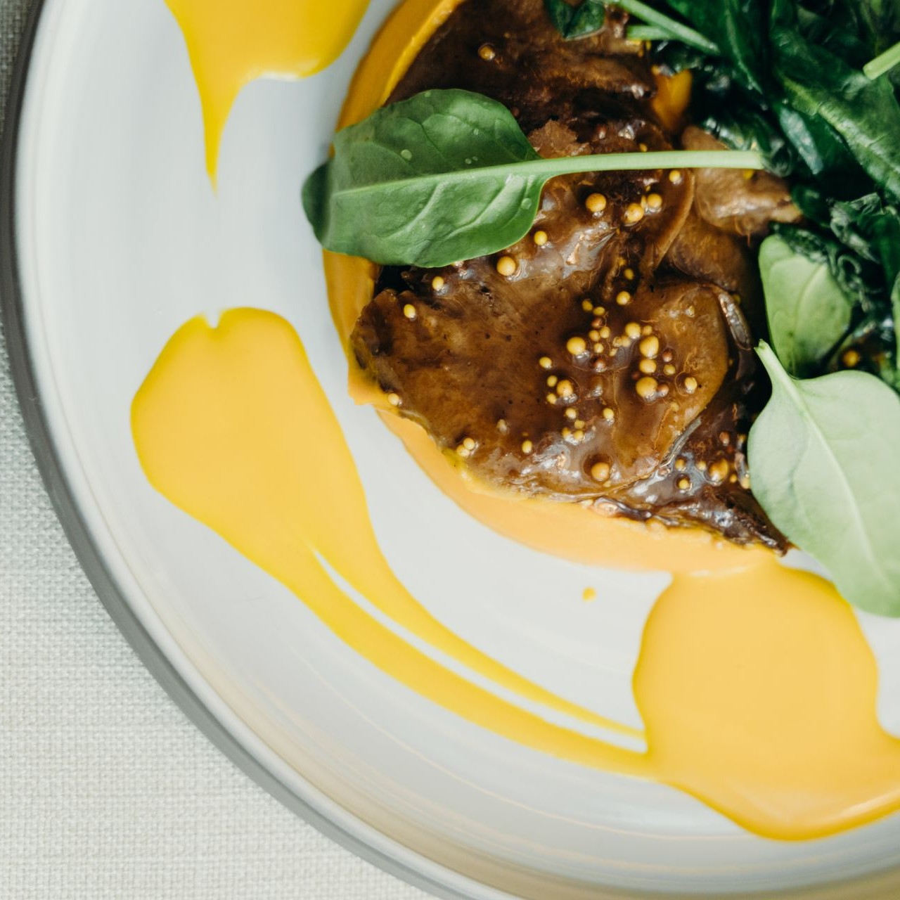 Gourmet Dish with Mustard Seeds Gourmet dish with mustard seeds, greens, and a yellow sauce pattern on a plate