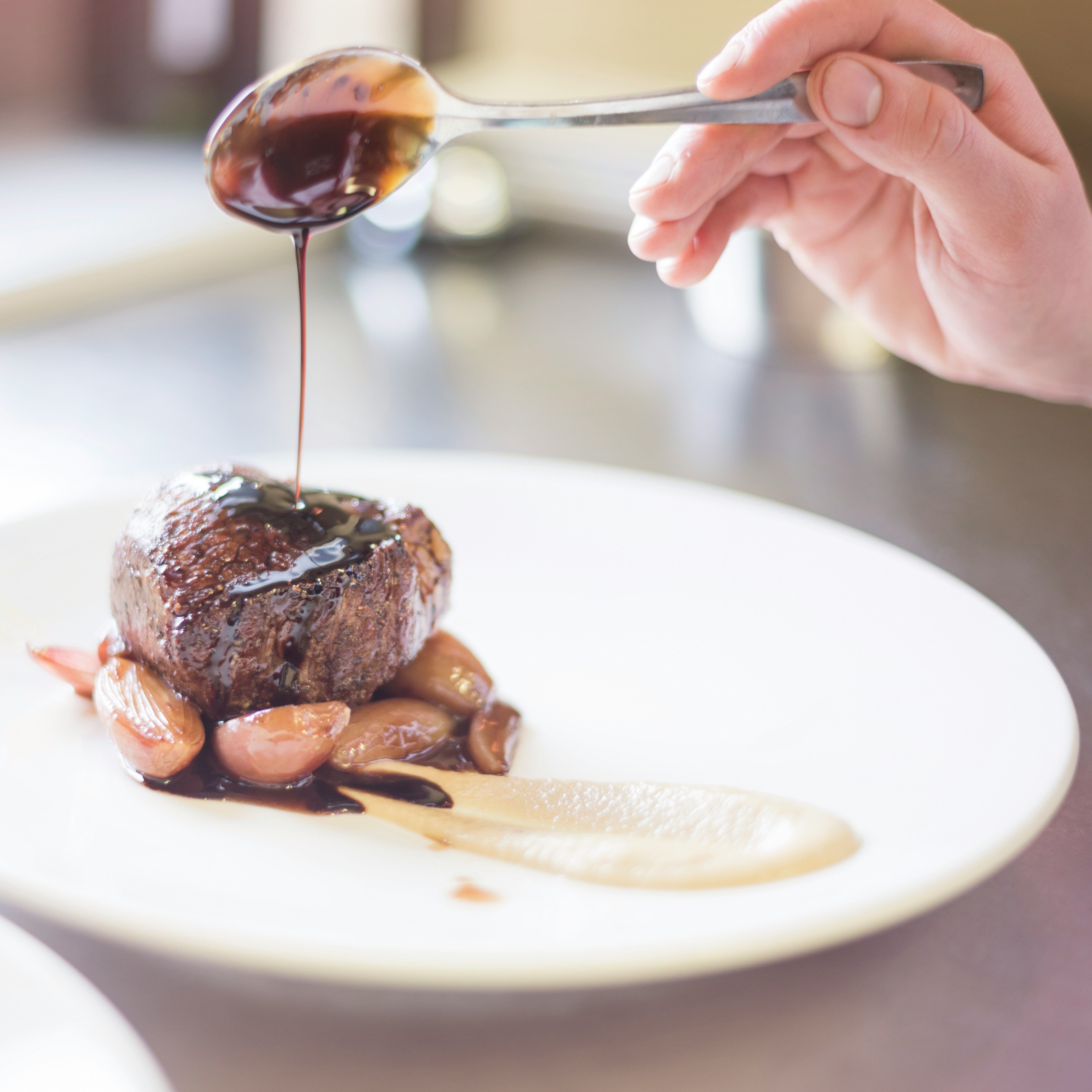 Gourmet Steak Presentation Chef drizzles sauce over a gourmet steak dish with shallots off-center on a plate
