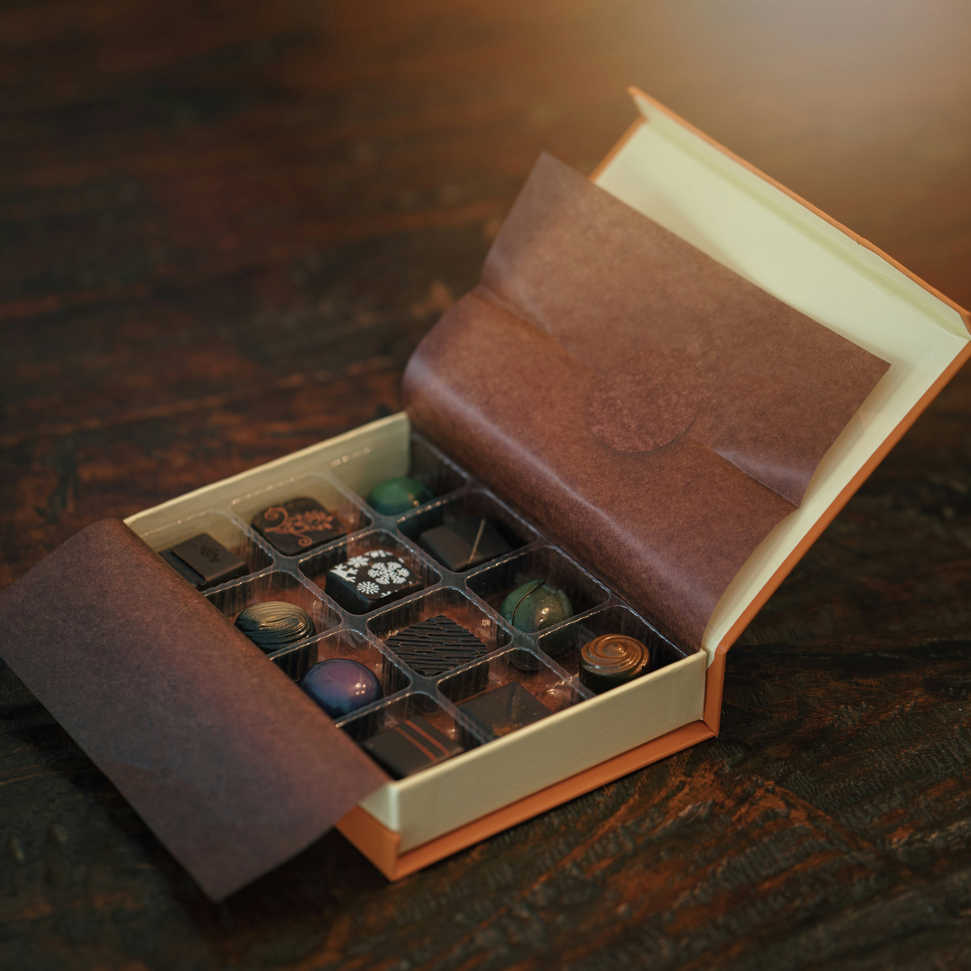 Assorted Chocolate Gift Box A box of assorted chocolates with decorative designs on a wooden table.