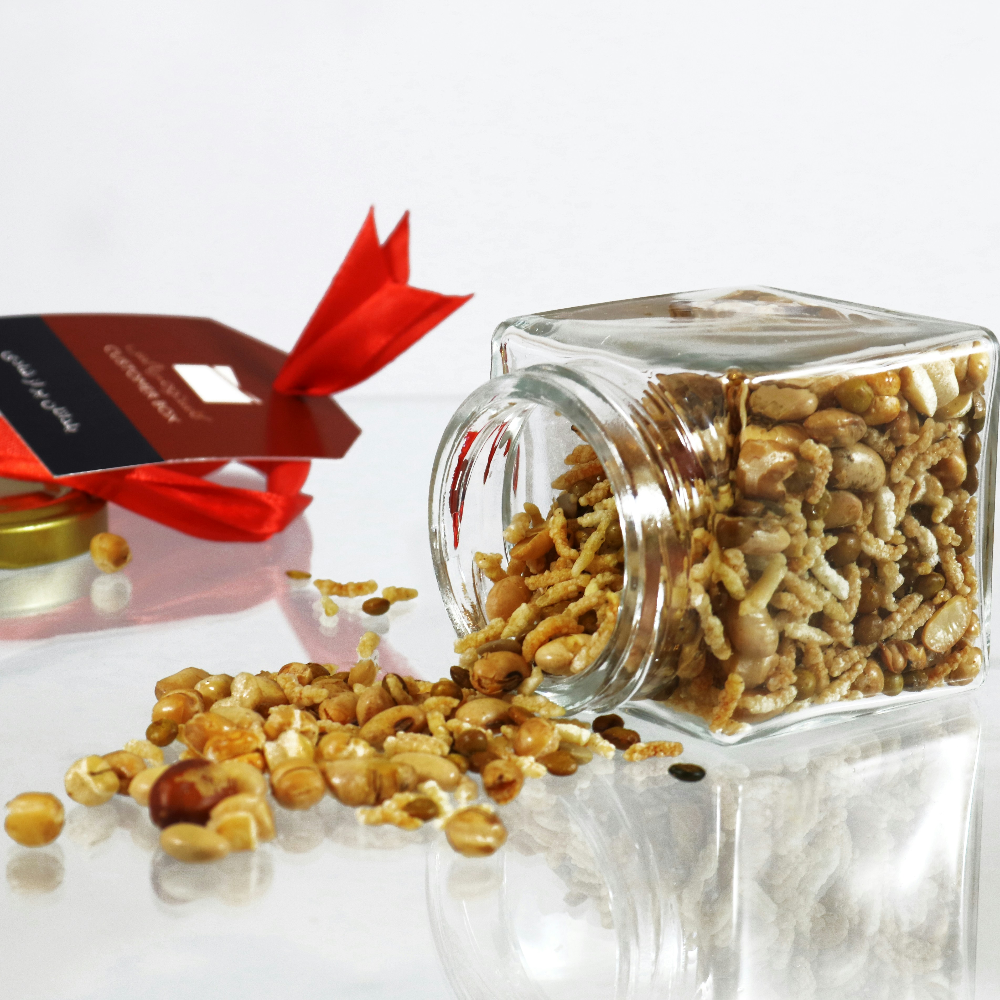 Mixed Nuts and Seeds Gift Jar A glass jar of mixed nuts and seeds spills onto a reflective surface.