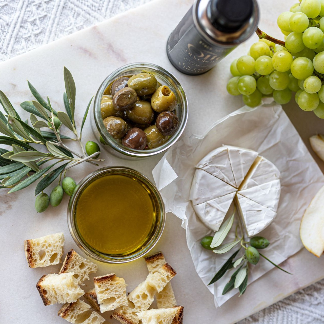 Assorted Edible Gifts Display Assorted edible gifts including olives, cheese, grapes, and olive oil on a marble surface