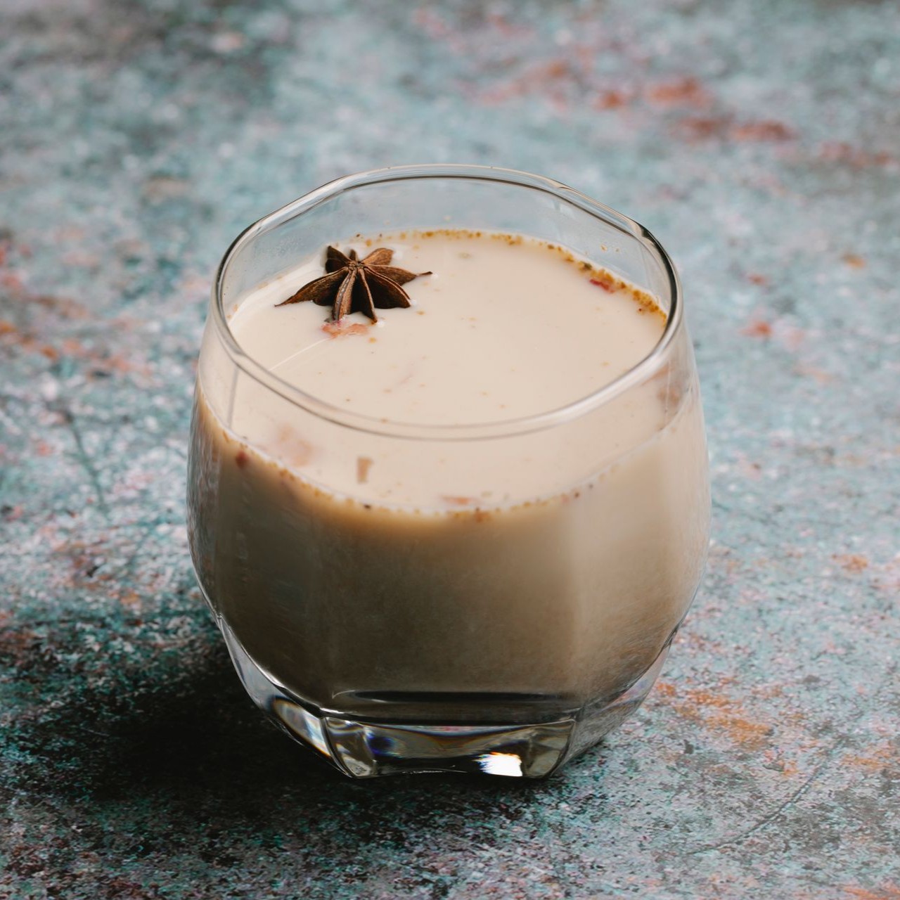 A creamy spiced chai in a glass garnished with star anise