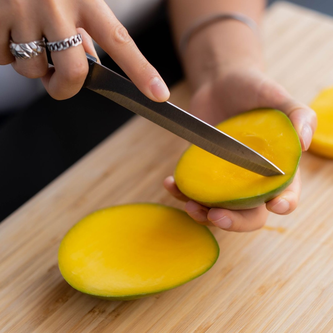 Slicing a Mango on Cutting Board Person slices a ripe mango on a wooden cutting board with a paring knife