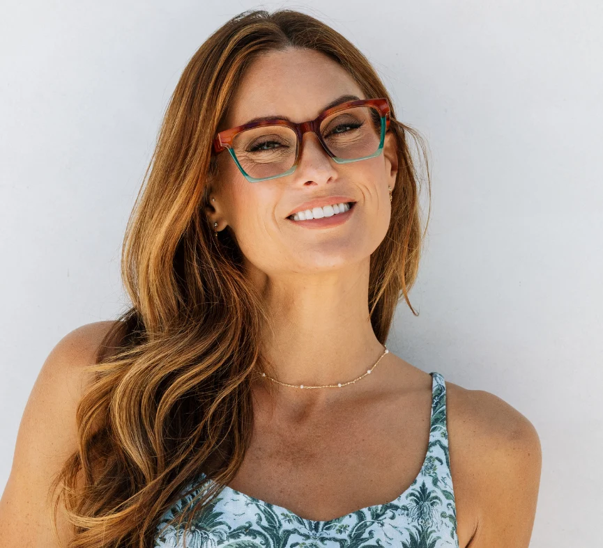 Woman with long hair and glasses smiles in a patterned top.