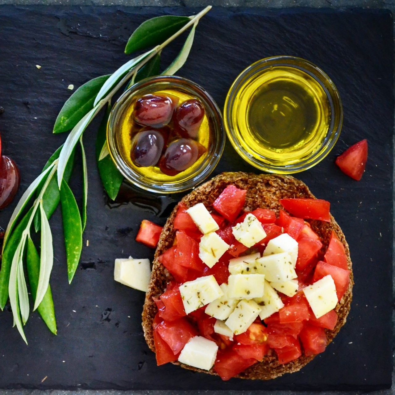 Award-Winning Olive Oils and Mediterranean Dish Olive oils and a Mediterranean dish with tomatoes and cheese on a slate board
