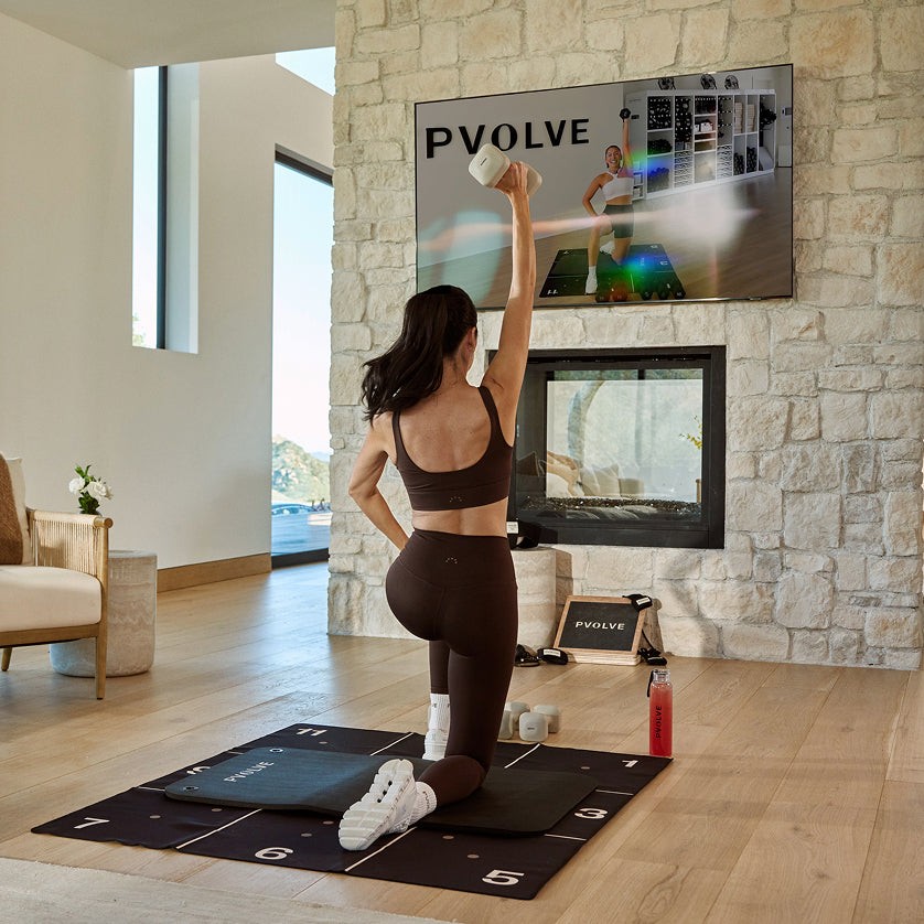 PVOLVE On Demand Workout A woman follows a PVOLVE workout on a TV in a modern living room