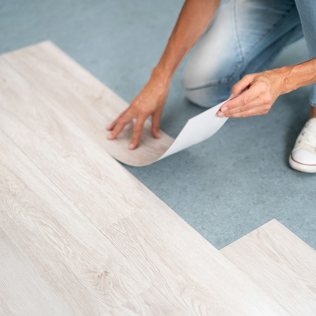 Person installing vinyl flooring on a blue surface
