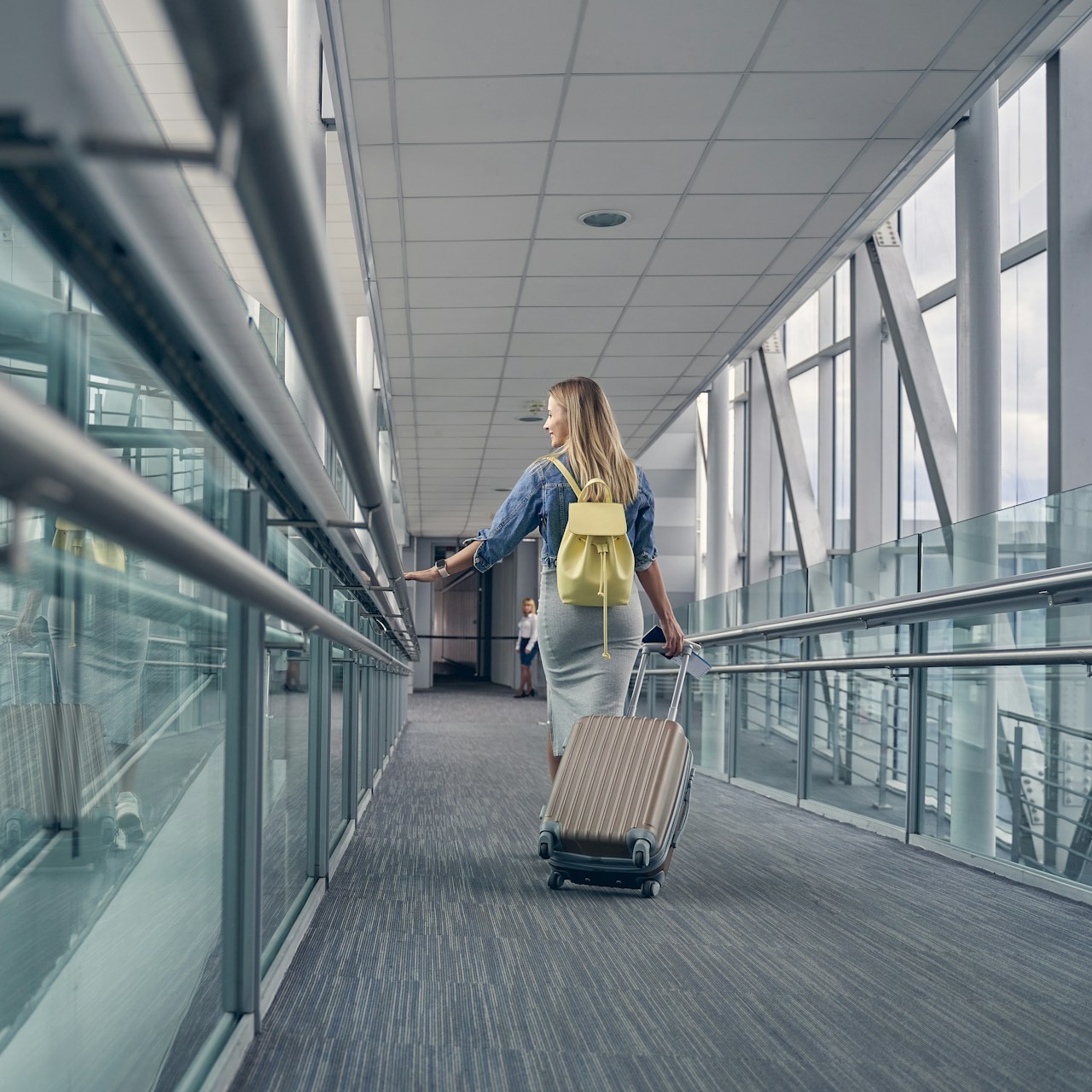 Traveler with Carry-On Luggage A woman walks through an airport terminal with a carry-on suitcase and a yellow backpack.
