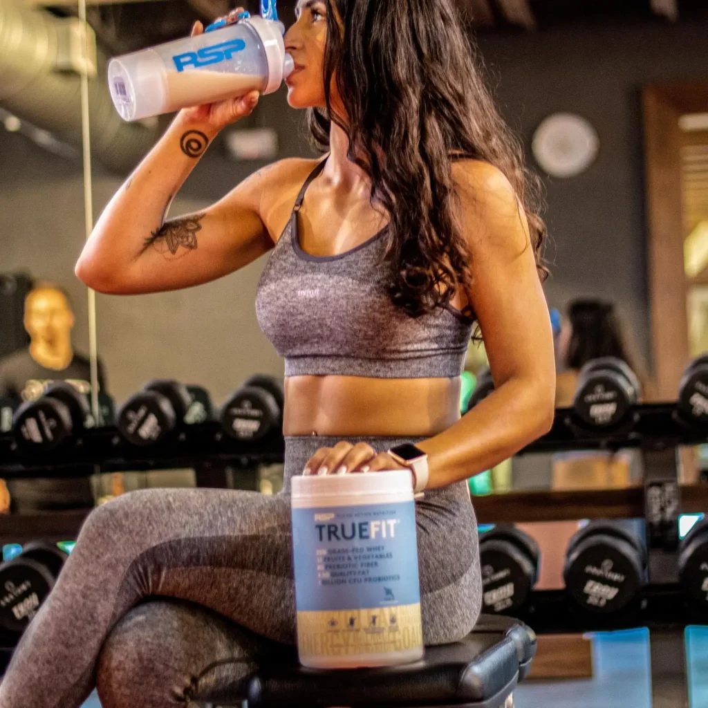 woman drinking truefit sitting on a gym bench woman drinking truefit sitting on a gym bench