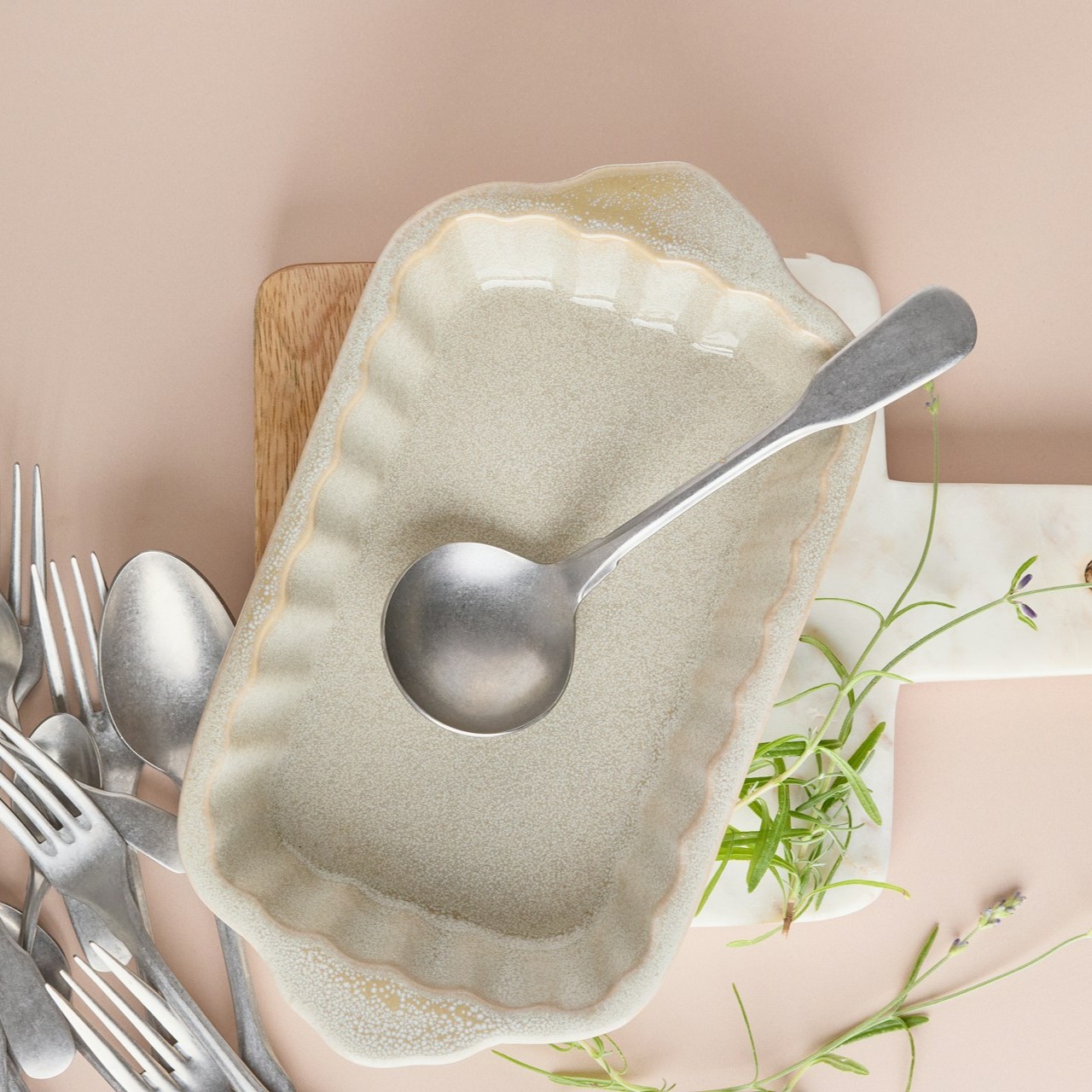 Ceramic Dish with Cutlery A ceramic dish with a ladle and cutlery arranged on a wooden board.