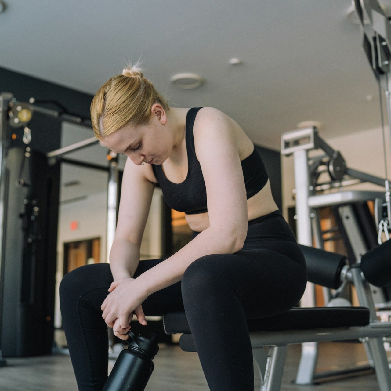 Woman Resting on Gym Bench Woman in workout attire sitting on a gym bench holding a water bottle